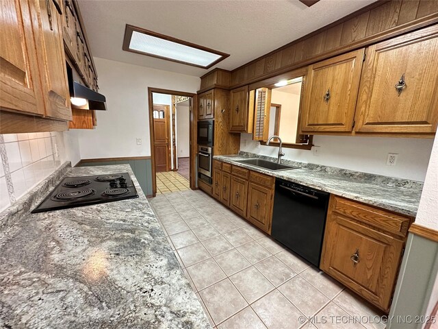 kitchen with black appliances, sink, light tile patterned floors, a textured ceiling, and light stone counters