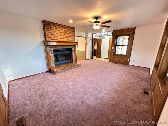 unfurnished living room featuring carpet, ceiling fan, a textured ceiling, and a brick fireplace