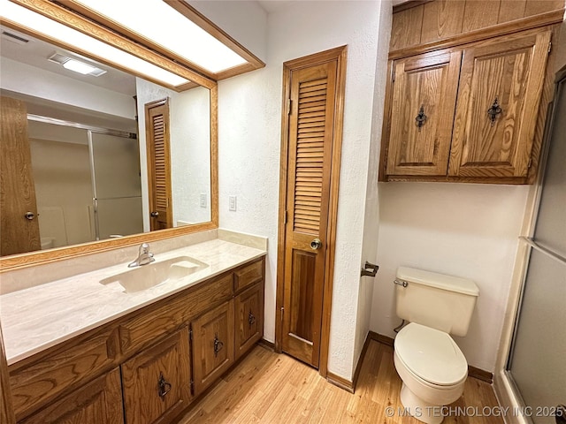 bathroom featuring hardwood / wood-style flooring, vanity, toilet, and a shower with door