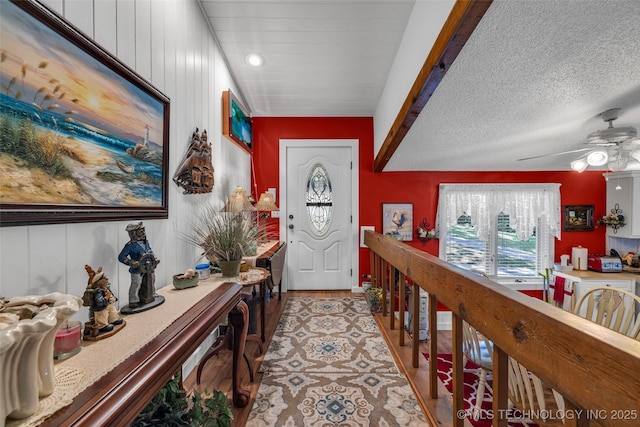 entryway featuring ceiling fan, a textured ceiling, and wooden walls