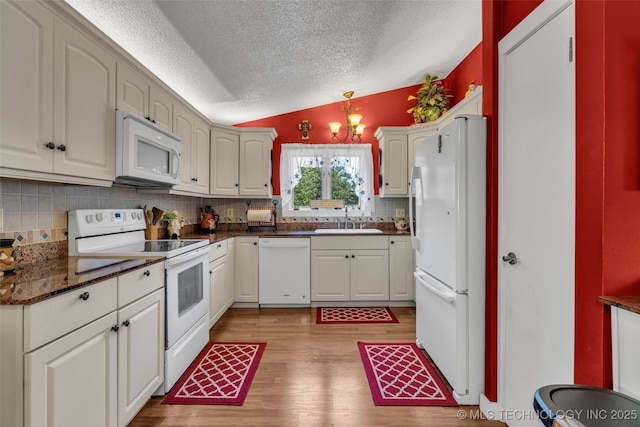 kitchen featuring sink, hanging light fixtures, lofted ceiling, white appliances, and white cabinets