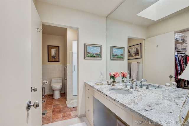 bathroom featuring vanity, toilet, tile walls, and a skylight