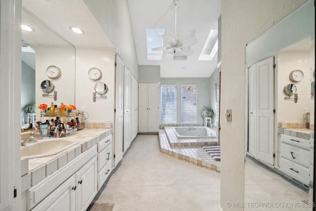 bathroom with vaulted ceiling with skylight, vanity, ceiling fan, and a bathing tub