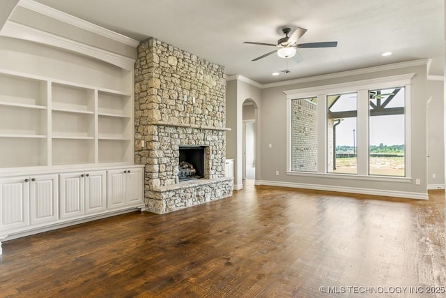 unfurnished living room with a stone fireplace, ceiling fan, dark hardwood / wood-style floors, built in shelves, and ornamental molding