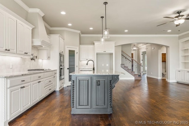 kitchen featuring a center island with sink, light stone countertops, decorative light fixtures, white cabinetry, and stainless steel appliances