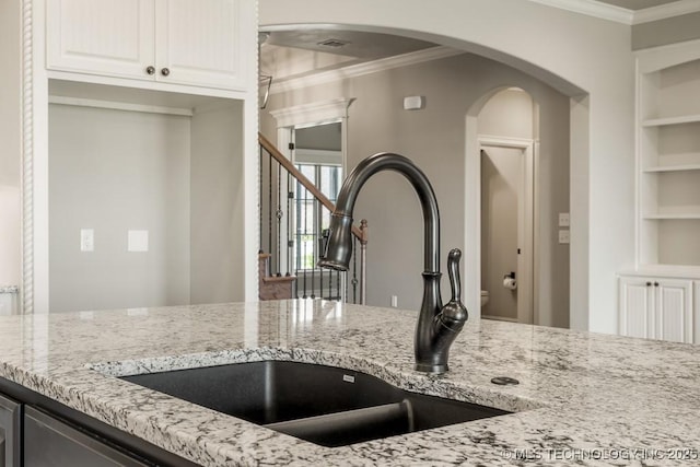 kitchen featuring white cabinets, crown molding, light stone countertops, and sink