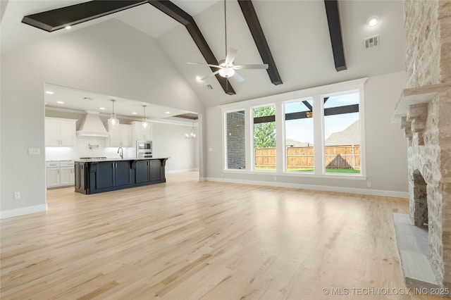 unfurnished living room featuring ceiling fan with notable chandelier, sink, high vaulted ceiling, a fireplace, and light hardwood / wood-style floors