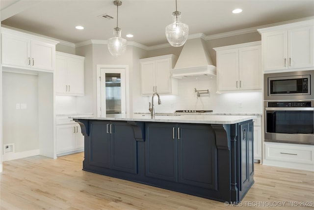 kitchen with appliances with stainless steel finishes, an island with sink, decorative light fixtures, white cabinets, and custom exhaust hood