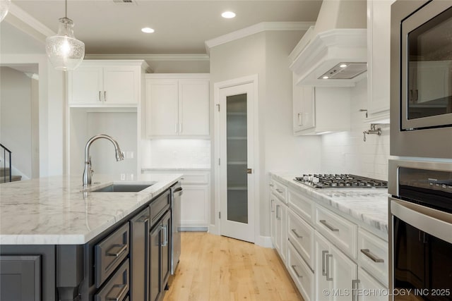 kitchen featuring sink, premium range hood, pendant lighting, white cabinets, and appliances with stainless steel finishes