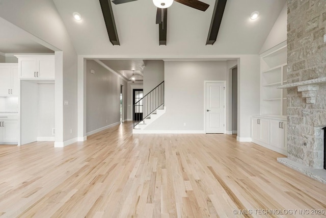 unfurnished living room with ceiling fan, a stone fireplace, built in features, lofted ceiling with beams, and light wood-type flooring