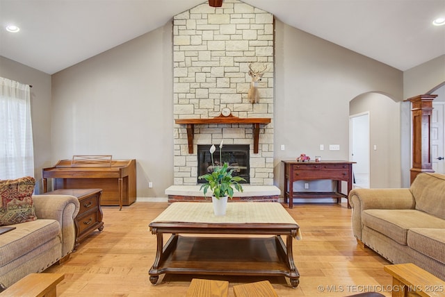 living room featuring a stone fireplace, high vaulted ceiling, and light wood-type flooring