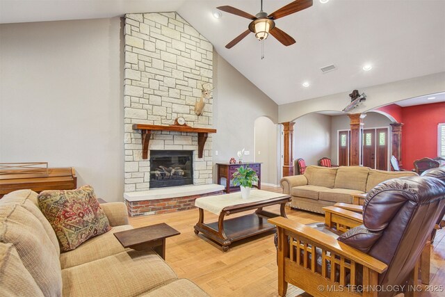 living room featuring ceiling fan, high vaulted ceiling, ornate columns, a fireplace, and light wood-type flooring