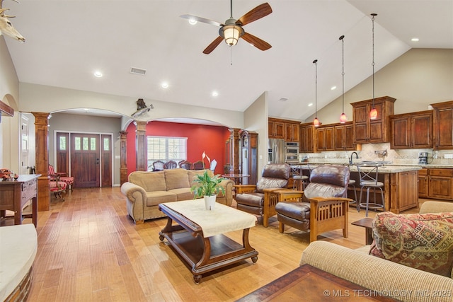 living room with ornate columns, high vaulted ceiling, sink, ceiling fan, and light wood-type flooring