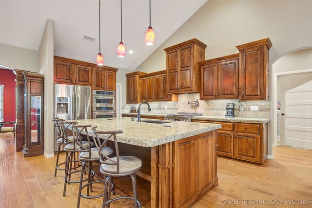 kitchen with decorative light fixtures, sink, stainless steel appliances, light stone countertops, and a center island with sink