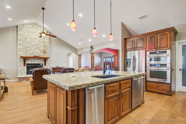 kitchen featuring sink, appliances with stainless steel finishes, an island with sink, pendant lighting, and a fireplace