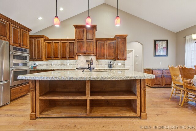 kitchen with decorative light fixtures, light stone countertops, and an island with sink