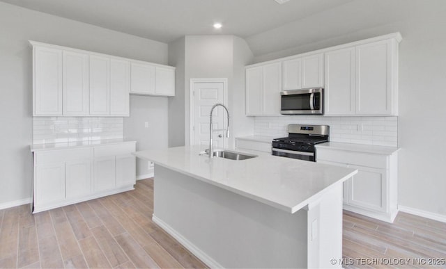 kitchen with a center island with sink, white cabinets, sink, tasteful backsplash, and stainless steel appliances