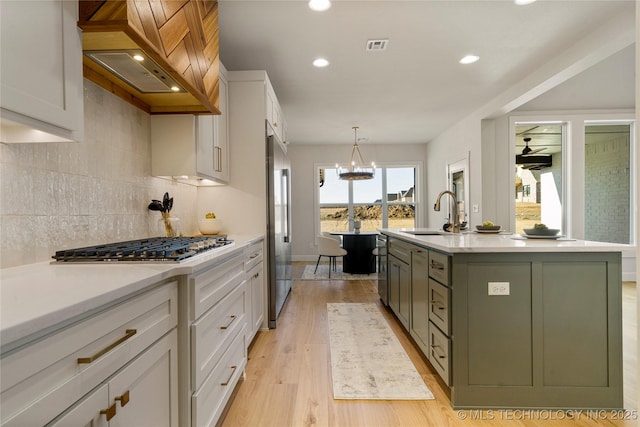 kitchen featuring premium range hood, white cabinets, sink, an island with sink, and stainless steel appliances