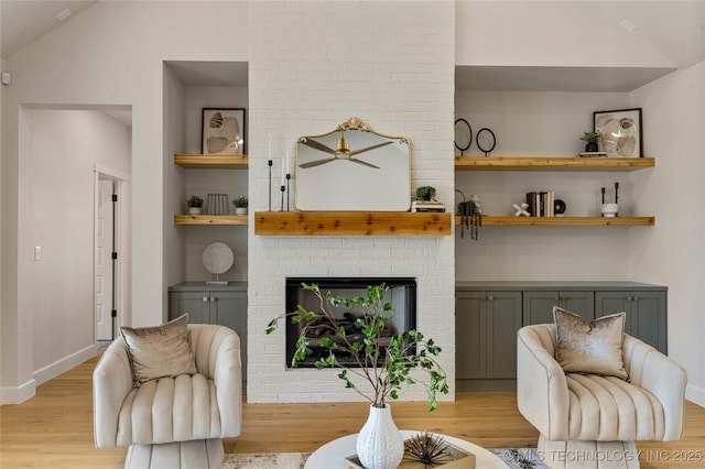 living room featuring built in shelves, ceiling fan, light hardwood / wood-style floors, vaulted ceiling, and a fireplace