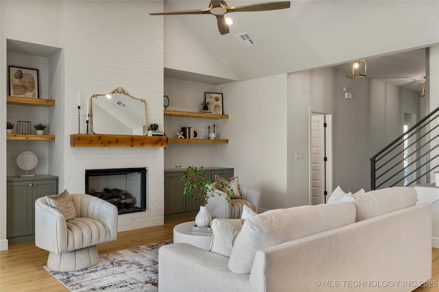 living room featuring a brick fireplace, ceiling fan, built in features, and light hardwood / wood-style flooring