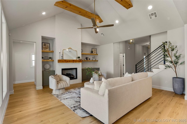 living room with a brick fireplace, ceiling fan, beam ceiling, high vaulted ceiling, and light hardwood / wood-style floors