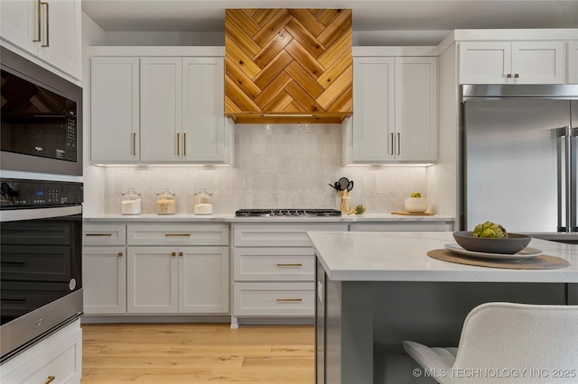 kitchen with white cabinetry, built in appliances, decorative backsplash, custom exhaust hood, and light wood-type flooring