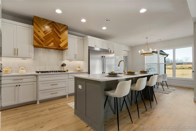 kitchen featuring backsplash, white cabinetry, stainless steel appliances, and an island with sink