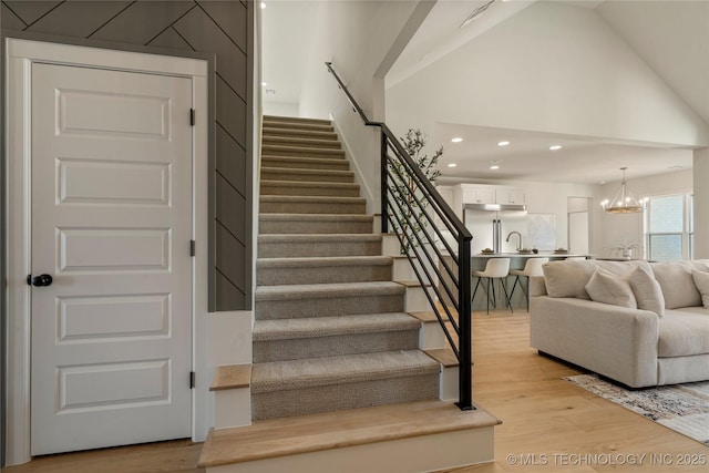 stairway with wood-type flooring, high vaulted ceiling, a notable chandelier, and sink