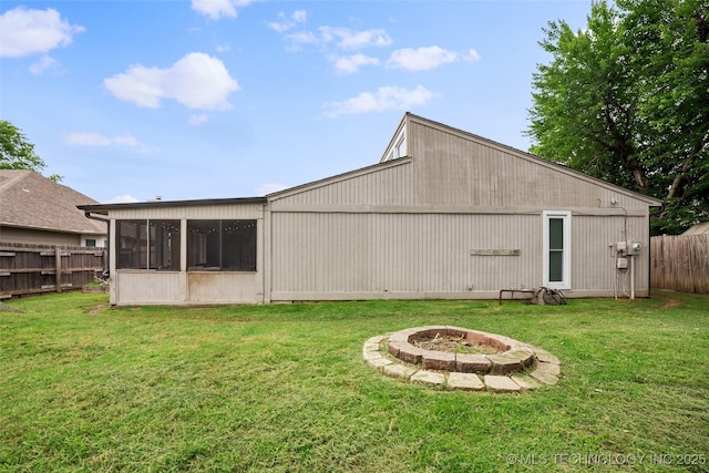 rear view of property with a fire pit, a lawn, and a sunroom