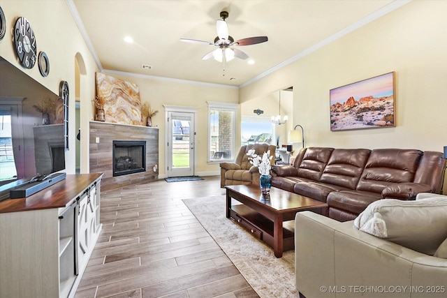 living room featuring ceiling fan with notable chandelier, ornamental molding, and a fireplace