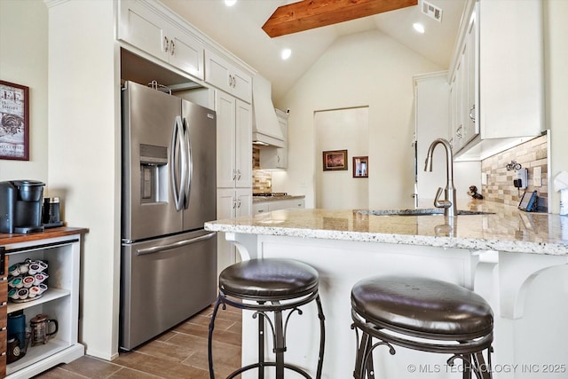 kitchen featuring vaulted ceiling with beams, appliances with stainless steel finishes, tasteful backsplash, light stone counters, and white cabinetry