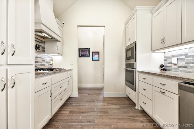 kitchen featuring stainless steel appliances, light stone counters, tasteful backsplash, and custom exhaust hood