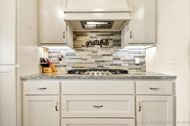 kitchen featuring stainless steel gas stovetop, custom exhaust hood, decorative backsplash, light stone counters, and white cabinetry