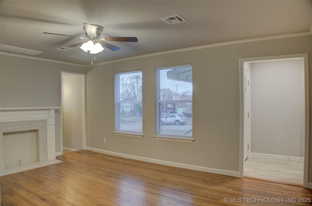 unfurnished living room with hardwood / wood-style floors, ceiling fan, crown molding, and a tiled fireplace