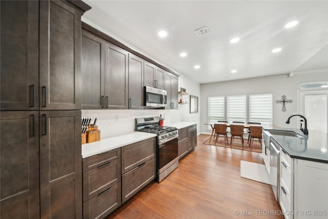 kitchen with sink, stainless steel appliances, crown molding, dark brown cabinets, and light wood-type flooring