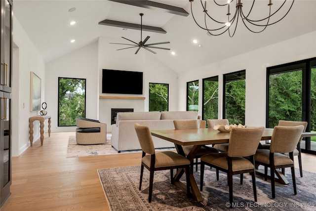 dining space with ceiling fan with notable chandelier, beam ceiling, light wood-type flooring, and high vaulted ceiling