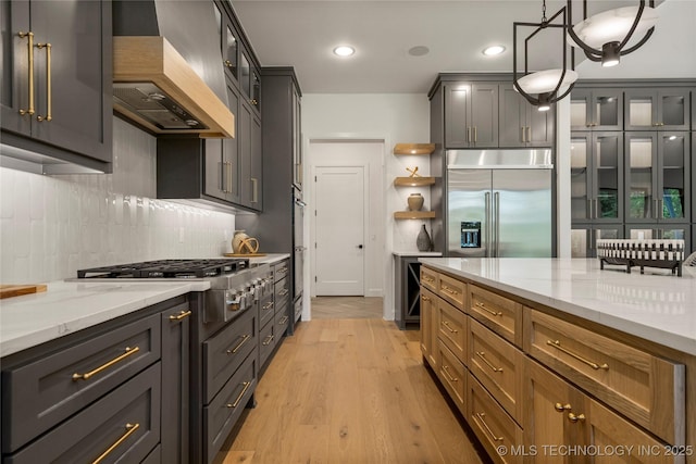 kitchen featuring light stone countertops, stainless steel appliances, light hardwood / wood-style flooring, decorative light fixtures, and custom exhaust hood