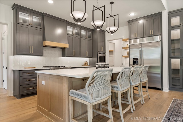 kitchen featuring custom range hood, stainless steel appliances, hanging light fixtures, and a center island with sink