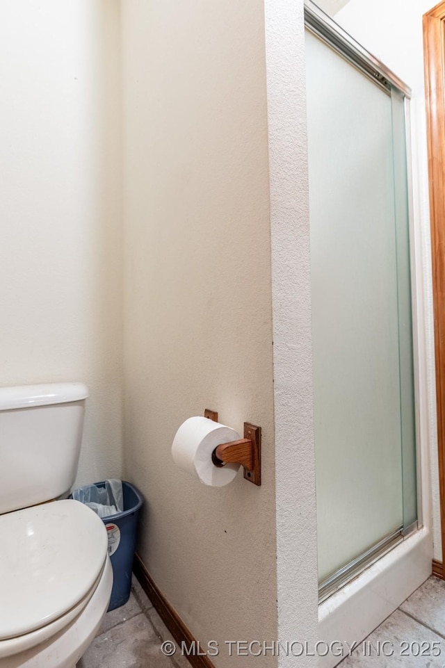 bathroom featuring tile patterned flooring, toilet, and a shower with shower door