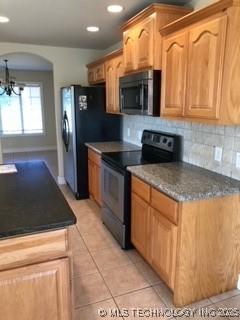 1704 Estates Dr, Grove, OK 74344 - kitchen with black range with electric stovetop, stainless steel microwave, light tile patterned flooring, arched walkways, and recessed lighting