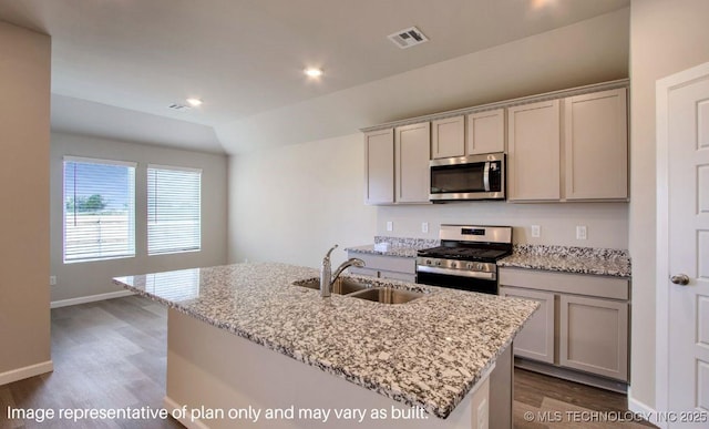 kitchen with stainless steel appliances, light stone counters, a kitchen island with sink, and sink