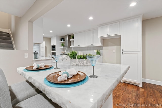 kitchen with white cabinets, wall chimney range hood, and dark wood-type flooring