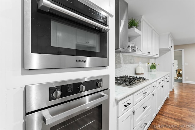 kitchen with dark wood-type flooring, decorative backsplash, light stone countertops, white cabinetry, and stainless steel appliances