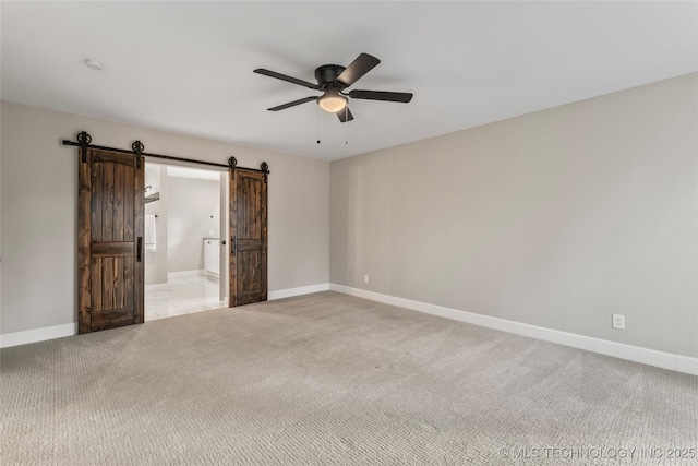 unfurnished bedroom with light carpet, a barn door, ensuite bathroom, and ceiling fan