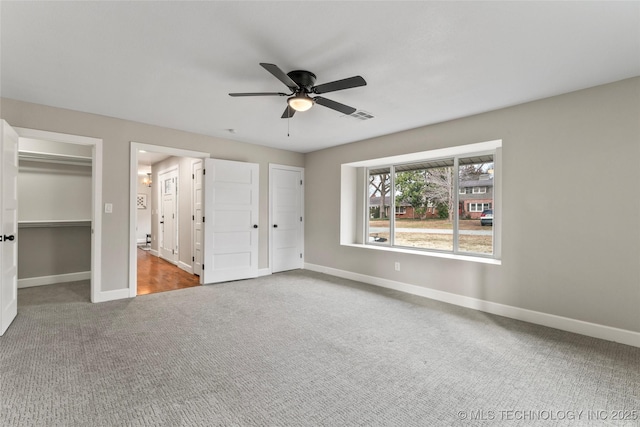 unfurnished bedroom featuring carpet, ceiling fan, and two closets