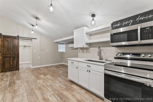 kitchen with vaulted ceiling, a barn door, appliances with stainless steel finishes, decorative light fixtures, and white cabinetry