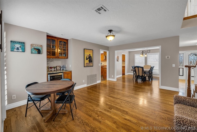 dining space with bar area, beverage cooler, a textured ceiling, and hardwood / wood-style flooring