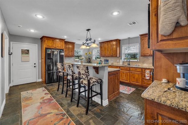 kitchen with a center island, a kitchen breakfast bar, stainless steel refrigerator with ice dispenser, decorative backsplash, and decorative light fixtures