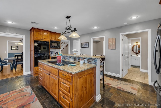 kitchen featuring a center island, black appliances, hanging light fixtures, light stone counters, and a breakfast bar area