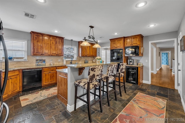 kitchen featuring pendant lighting, a center island, black appliances, light stone counters, and beverage cooler